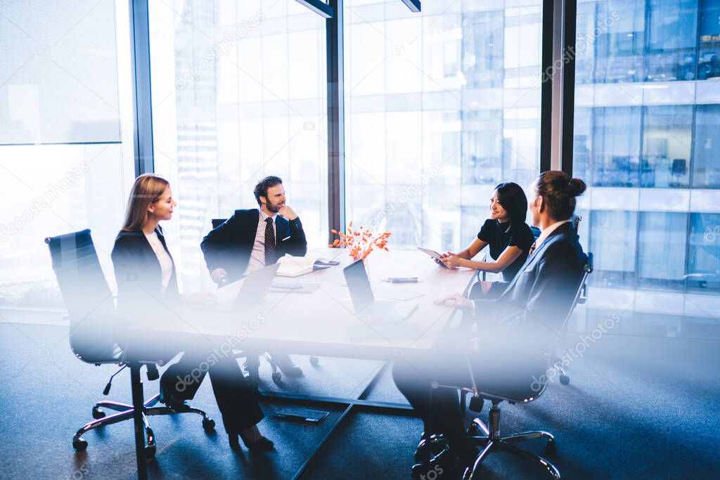 Concept of brainstorming and briefing, positive diverse male and female financial experts discussing information during working time in conference room sitting at desktop with laptop devices