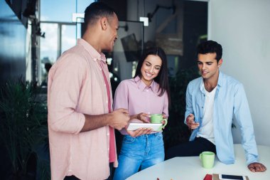 Neşeli çeşitli erkek ve kadınlar ofis içi iş günlerinde modern dokunmatik ped üzerinden komik web videoları izliyorlar, olumlu genç çalışanlar online iletişim için teknolojiyi kullanıyorlar.