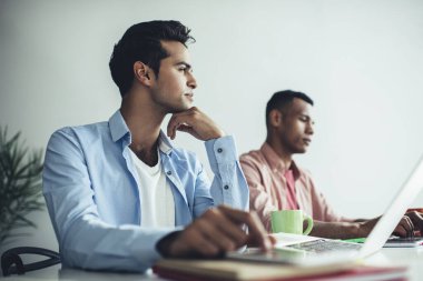 Düşünceli bir adam, başlangıç ve veritabanı fikrini düşünürken düşünceli bakışlarını başka yöne çeviriyor. Modern laptop cihazıyla masaüstünde oturuyor. Erkek yazılım geliştirici uygulamayı güncelleme üzerine kafa yoruyor.