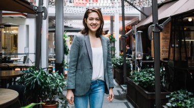 Gri ceketli, başında güneş gözlüğü olan çekici Asyalı kadın rahat kafenin yanında kameraya bakıyor ve gülümsüyor.