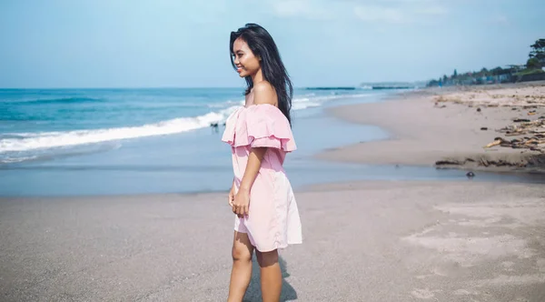 身穿粉色太阳衣的印度尼西亚年轻女子微笑着在巴厘岛海滨漫步 在阳光下微笑着离去的侧影 — 图库照片