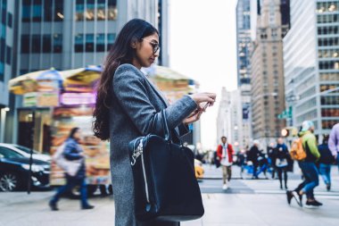 Gözlüklü genç iş kadını New York 'un işlek caddesinden geçerken cep telefonu kullanıyor.