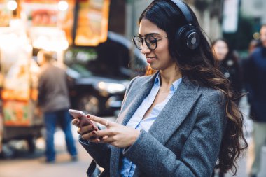Ofisteki neşeli genç kadın, kulaklık ve cep telefonuyla müzik dinlemekten zevk alıyor.