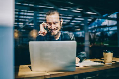 Arkadaşlarıyla akıllı telefondan konuşan başarılı öğrencilerin portresi, ücretsiz 4G kullanarak şık kahve dükkanlarının içinde e-öğrenim sırasında internet sitelerinde bilgi edinmek için dizüstü bilgisayarla otururken.