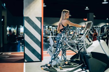 Spor kıyafetli genç sarışın bir kadının spor salonundaki spor değirmeninde spor yaparken sağlıklı vücut bakımı yaparken yan görüntüsü.