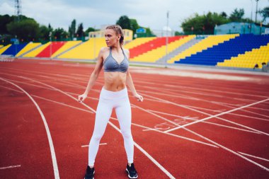 Beyaz taytlı, gri bluzlu, kendine güveni tam bir kadın koşan kırmızı pistte duruyor ve antrenman sırasında gözlerini başka yöne çeviriyor.