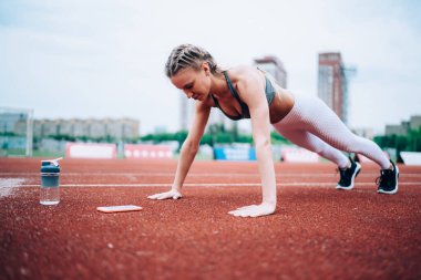 Spor giyim sektöründe aktif ve sportif bir bayan arka planda kırmızı piste, akıllı telefon ve bir şişe su itiyor.