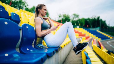 Beyaz tozluklu, gri tişörtlü, spor ayakkabılı ve stadyumda mesajlaşırken yüzünü çeviren güzel bir kadın.