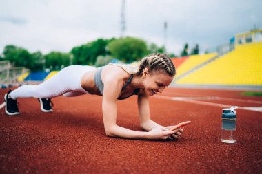 Sarışın, at kuyruklu çekici ve neşeli bir bayan stadyumda tahta örgü örüyor ve sosyal medyada bulanık arka planda gezinirken gülümsüyor.