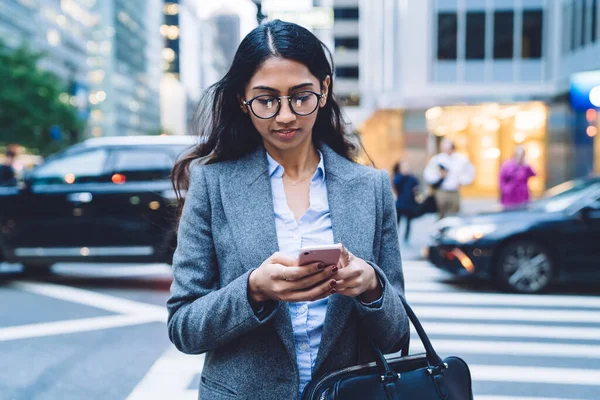 ニューヨークの道路を横断しながらメガネとグレーのジャケット携帯電話でブラウジングの美しいEthniビジネス女性 — ストック写真