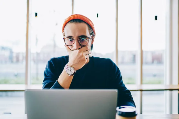 Shocked young hipster guy in spectacles amazed with 4G connection watching webinar online on netbook, surprised caucasian male shocked with received email about web store sales on laptop computer