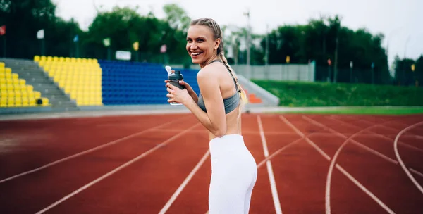 若いです魅力的なフィット女性アスリートスポーツウェアでカメラを見て笑いながらスタジアムのトレッドミルの背景に立って — ストック写真