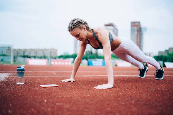 スマートフォンの近くの赤いトラックを上に押すスポーツウェアのアクティブとスポーティーな女性とぼやけた背景に水のボトル — ストック写真