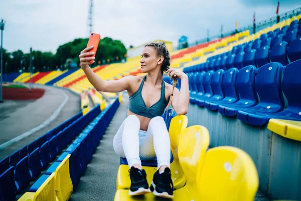 Yetişkin Atletik Kadın Stadyumdaki Tribünün Sandalyesinde Otururken Akıllı Telefondan Fotoğraf — Stok fotoğraf