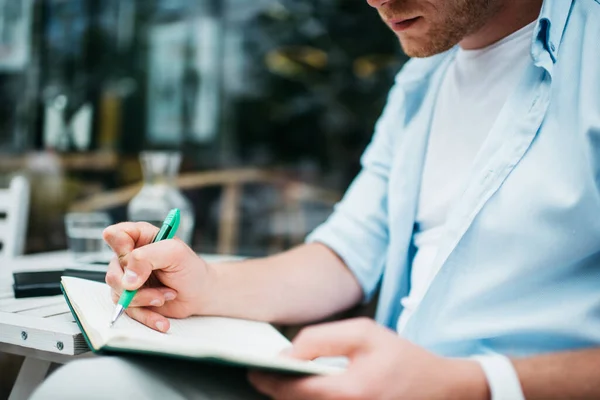 穿着蓝色衬衫的千禧年作物人坐在桌旁 在街边咖啡馆的阳台上用空白记事本记笔记 — 图库照片
