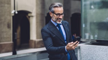 New York 'ta cep telefonunu kullanarak şeffaf balkonda duran takım elbiseli ve gözlüklü mutlu orta yaşlı işadamı.