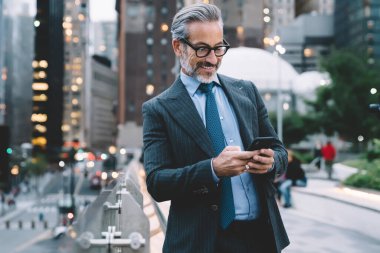 Yakışıklı, gri saçlı, sakallı iş adamı siyah takım elbiseli, mavi kravatlı ve gözlüklü New York 'ta cep telefonuyla mesajlaşan.