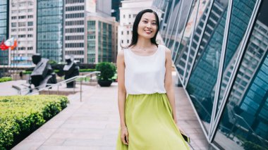 Beyaz bluzlu ve limonlu güzel Asyalı kadın şehir merkezinde modern binanın yanında yürürken kameraya bakıyor.