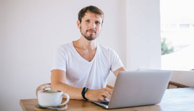 Modern dizüstü bilgisayarda uzaktan çalışan, kahve dükkanında oturan, kablosuz ücretsiz 4G internete bağlı, uzaktan kumandalı, yakışıklı erkek serbest çalışanın portresi.