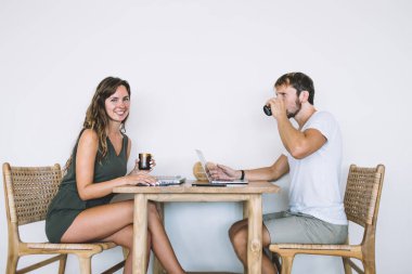 Yetişkin, yakışıklı, sakallı, günlük giysiler giymiş, kafeteryada beyaz arka planda giyinmiş neşeli, güzel bir kadının önünde meyve suyu içen bir erkek.