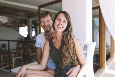 Güzel görünümlü, şık giyinmiş, halka açık kafeteryada boş zamanlarında oynaşan mutlu evliliğin portresi pencerenin kenarında oturup kameraya gülen güzel bir çift.