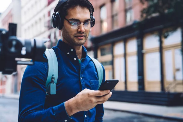 Confident Attractive Ethnic Casual Adult Man Earphones Eyeglasses Backpack Texting — Stock Photo, Image