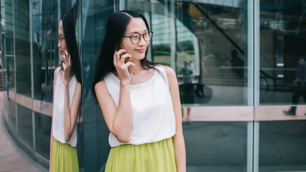 Nöjd Asiatisk Kvinna Glasögon Med Smartphone Handen Står Bredvid Glasvägg — Stockfoto