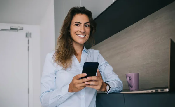 Ganska Optimistisk Kvinna Blå Skjorta Står Med Smartphone Hemma Och — Stockfoto