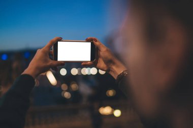 Tanımlanamayan kadın fotoğrafçı elinde modern cep telefonuyla boş ekrana bakarak şehrin gece fotoğraflarını çekiyor.