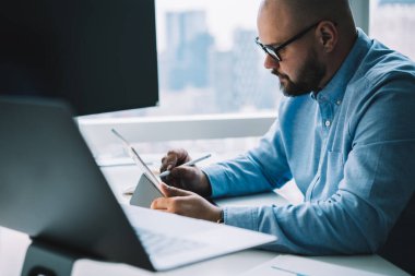 Bilgisayarda bilgisayarın başında dizüstü bilgisayarla otururken grafik tablet üzerinde çalışan odaklanmış sakallı adamın ekin kenarı görüntüsü