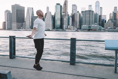 Genç, kısa saçlı, kulaklıkla müzik dinleyen, metal tel örgülerin yanında ip atlayan etnik bir adamın yan görüntüsü.