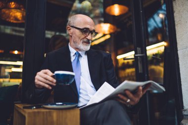 Sakallı, kahve fincanı bardaklı ve takım elbiseli, camlara gazete okuyan yakışıklı adam.