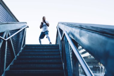 Tişörtlü, siyah eldivenli, kel, Afro-Amerikan bir boksörden şehrin açık gökyüzüne karşı gölgelerde boks maçı.