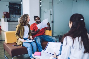 Modern çok ırklı kadınlar ve erkek modern ofiste koltukta oturuyor ve takım halinde proje planı üzerinde çalışırken gazete okuyor. 
