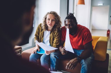 Modern iletişim çok ırklı erkek ve kadın gazeteleri koridorda kanepede oturuyor ve grup arkadaşlarıyla konuşuyor.