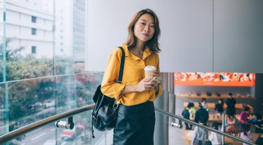 Halka açık yerlerde cep telefonu ve kahve ile poz veren güzel hippi kız portresi. Deri etekli ve sırt çantasıyla kameraya bakan modaya uygun giyinmiş kadın.