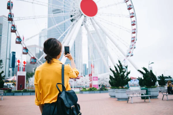 身着休闲装 背着智能手机的成年黑发女子的背景图 她在市区游乐园拍下了摩天轮的照片 — 图库照片