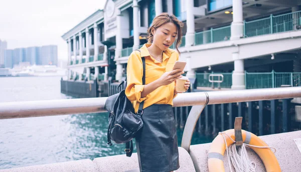 令人惊讶的是 在香港的渡口码头 亚洲女性身穿黄色衬衫 穿着黑色皮裙 背包在手机上打字 嘴巴张开 — 图库照片
