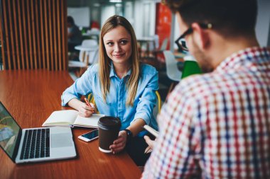 Kişisel planlayıcı ve modern aletler, gülümseyen bir kadının yanında, pozitif iş kadınına bakan kahve bardağı tutan ve ders kitabına not aldığı için arkadaşından bilgi alan biri.