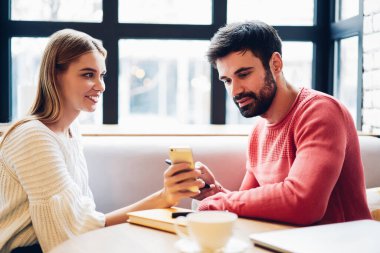 Gülümseyen milenyum çifti birlikte akıllı telefon kullanıyor web sitesinde medya videoları izliyor, mutlu sevgili sosyal ağları kontrol ediyor, genç kadın erkeğe yeni cep telefonu uygulaması gösteriyor