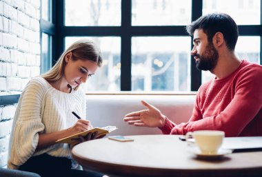 Kafe içinde oturan ve iletişim kuran, zeki karı-koca bütçeyi kontrol eden sakallı bir adamla yaptığı görüşme sırasında ders kitabına not tutan beyaz tenli çekici bir kadın gazeteci.
