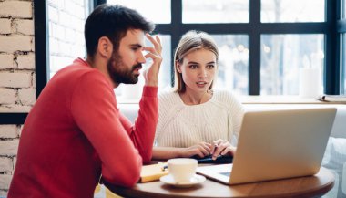 Ciddi erkek ve kadın girişimciler, web sitesinde bilgi okurken ortak proje detaylarını tartışarak kapalı alanlarda iş birliği yapıyorlar, program kodları üzerinde uzaktan beyin fırtınası yapan yetenekli serbest meslek sahipleri,