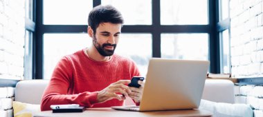 Akıllı telefondan arkadaşından mesaj okuyan genç bir adam dizüstü bilgisayarla birlikte şık bir çalışma alanında oturuyor, yetenekli bir serbest yazar cep telefonuna ücretsiz internet bağlantısı üzerinden yeni bir uygulama yüklüyor