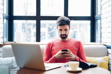 Milenyum erkeği akıllı telefonu elinde tutuyor. Bilgisayarda işlem yaptığını doğrulayan bir mesaj alıyor. Cep telefonu uygulamasını kullanarak verileri bluetooth bağlantısı üzerinden netbook ile senkronize ediyor.