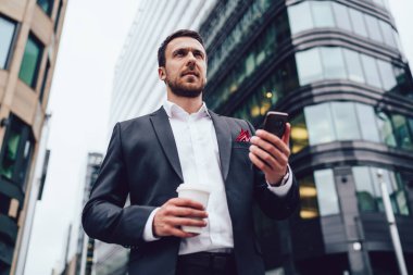 Finans bölgesinde kahve molası sırasında elinde cep telefonu bulunduran düşünceli, deneyimli bir erkeğin bakış açısının altında profesyonel danışmanlık için bekleyen düşünceli bir adam.