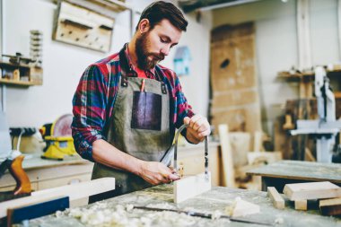 Profesyonel el sanatları ustası, restorasyon üretiminde boş zamanlarında ahşap inşaatı yapıyor. Önlüklü beyaz adam atölyedeki mobilyaların geliştirilmesi üzerine yoğunlaşmış.
