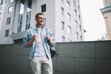 Kot ceketli, sırt çantalı ve tek kullanımlık kahveyle sokağa bakan modern ilham verici adamdan.