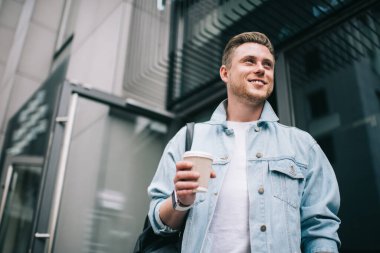 Kot ceketli, esinlenilmiş milenyum erkeğinin kahvesini yudumlayarak sokağa çıkıp gülümsemesinden.