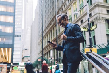 Gözlüklü ve koyu renk takım elbiseli orta yaşlı işadamının New York sokaklarında akıllı telefon yumruğunu ikiye katlaması.
