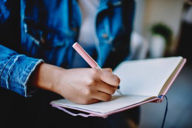 Kişisel günlüğe kalem yazma düşüncesi olan kadın ellerinin kırpılmış görüntüsü, üniversite ders kitapları, öğrenim ve öğrenim konsepti ile ilgili bilgileri not alıyor